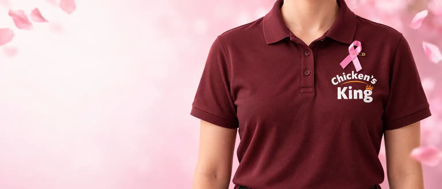 Un équipier en polo bordeaux Chicken's King portant le ruban rose, parmi des pétales roses